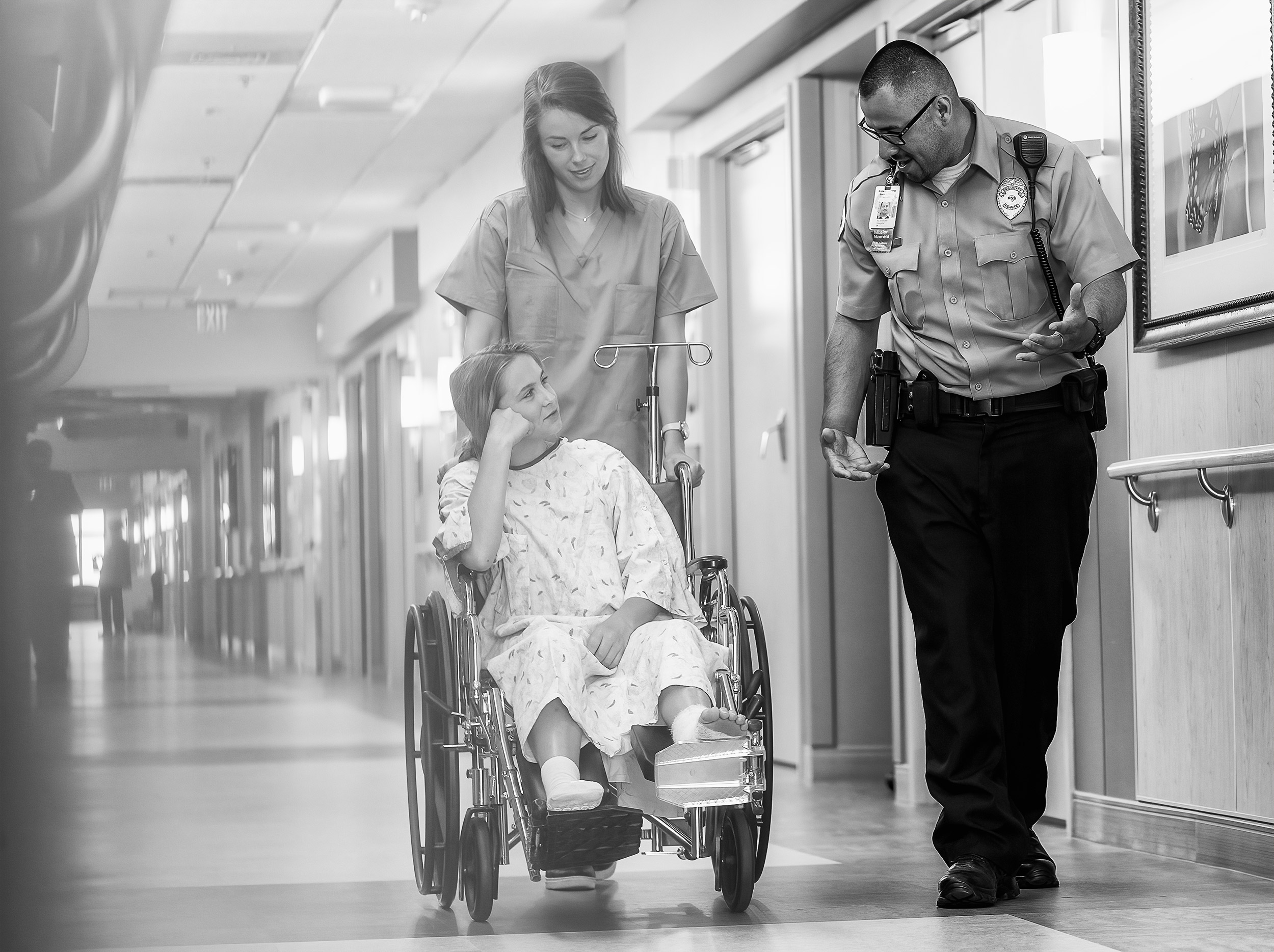 Nurse pushing patient in wheelchair down hallway escorted by security guard for HSS advertising. 