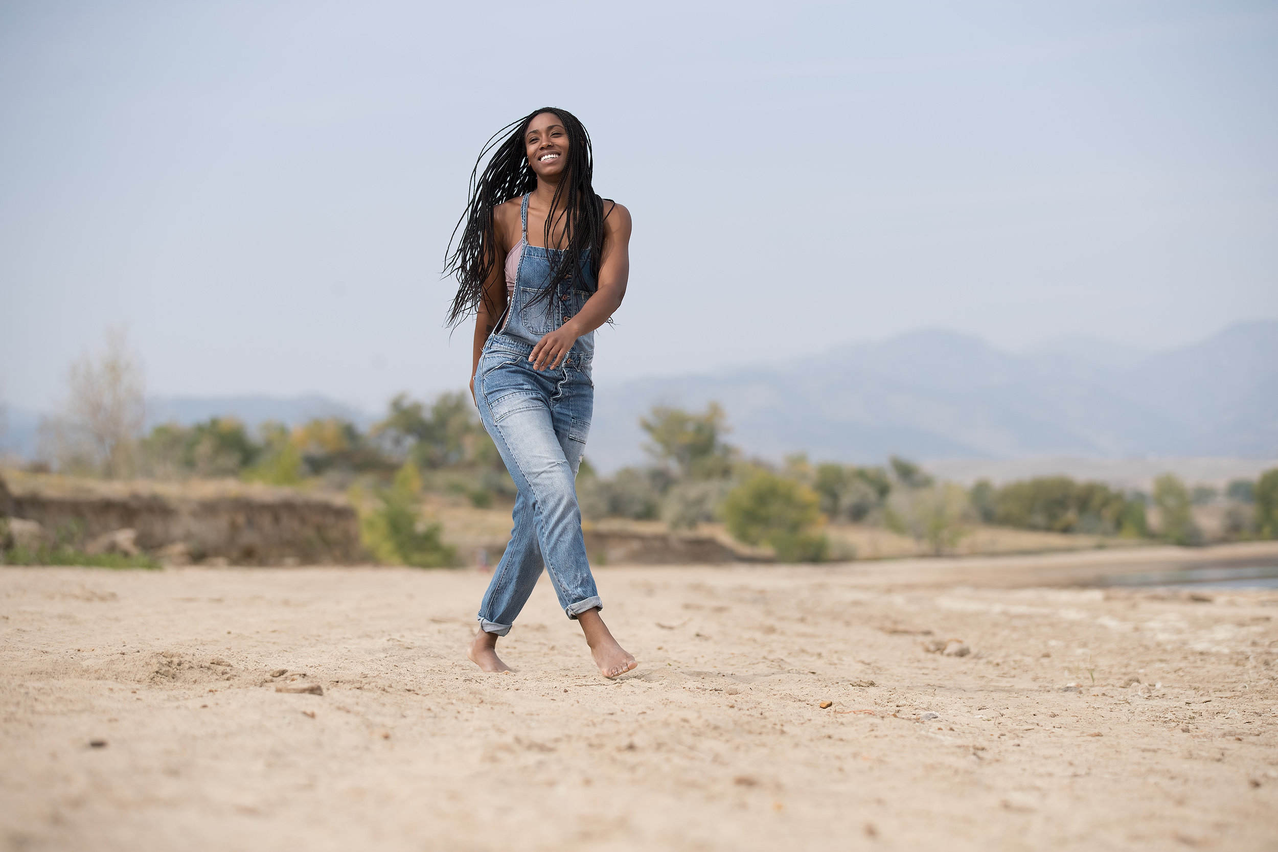 Female model walking on sand near lake with overalls 