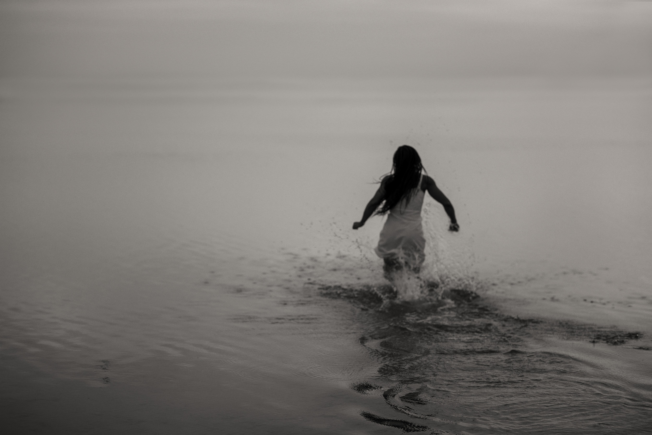 Black and white photo of a woman running into a lake