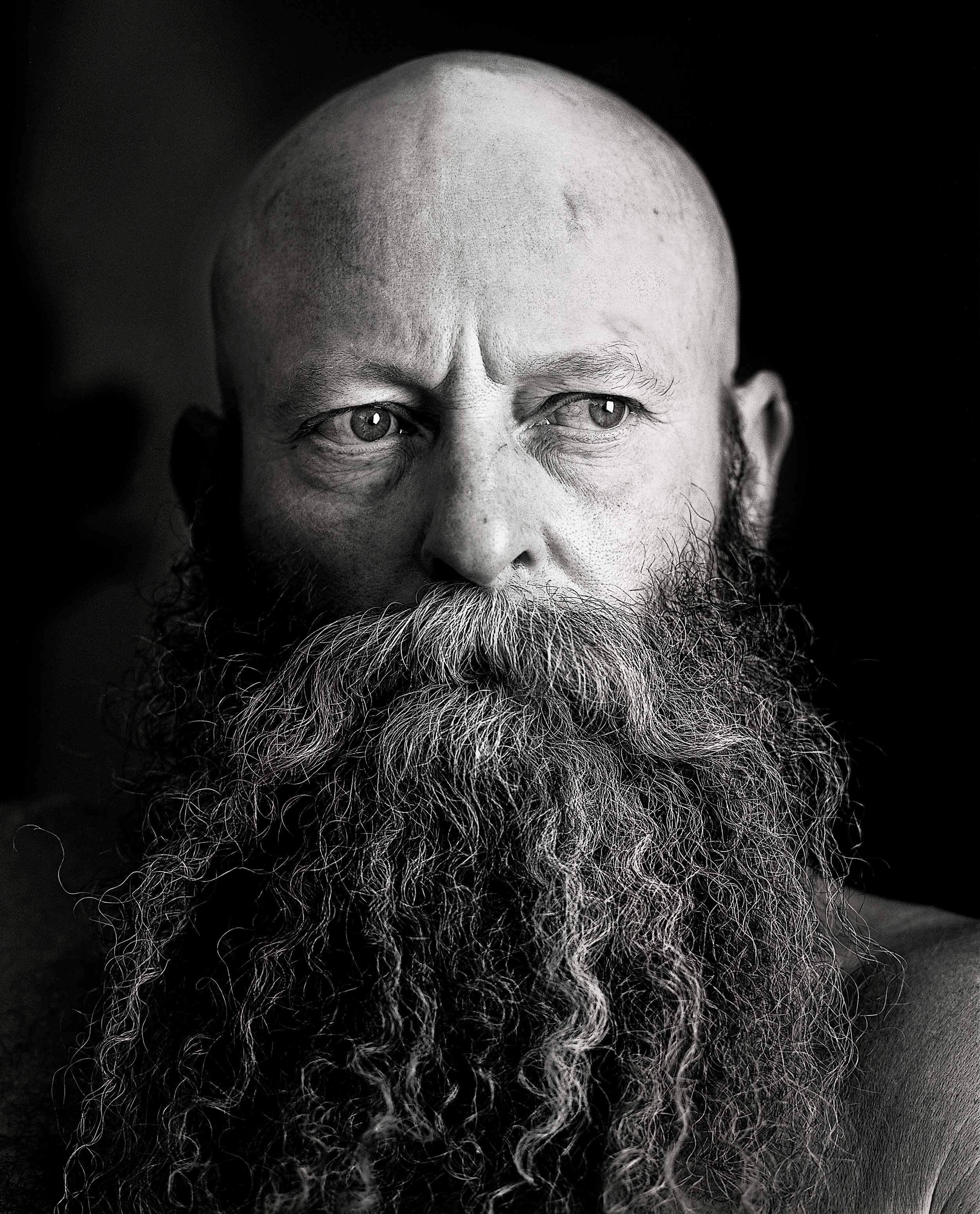 Black and white photo of a bearded bald man close up