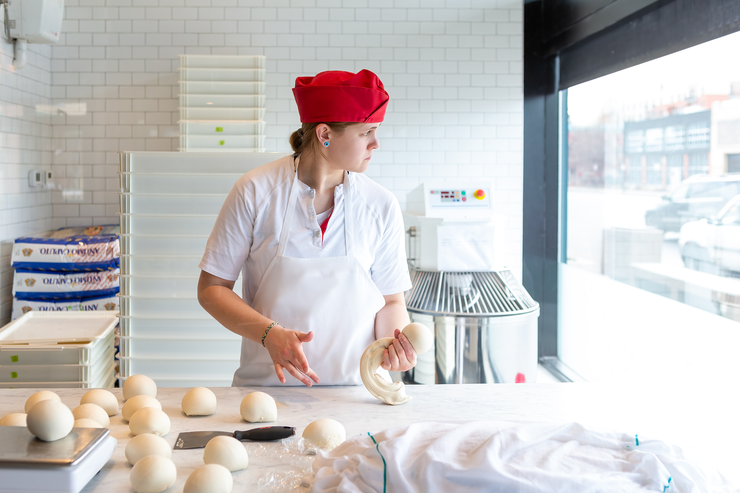 Baker rolling pizza dough on slab near a window with morning natural light for Pizzaria Locale.