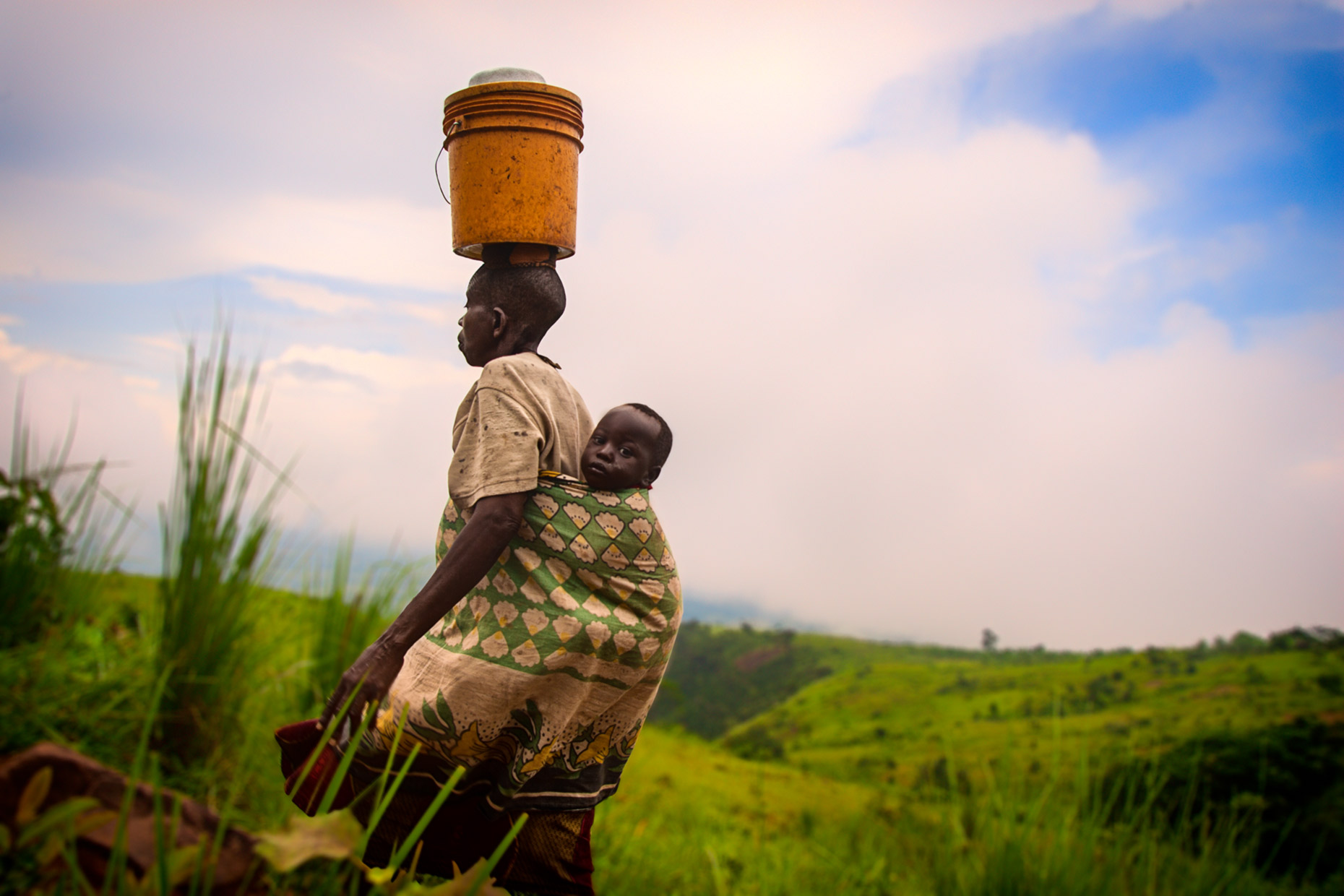 Tanzanian mother with baby carrying water bucket. Agriculture photography