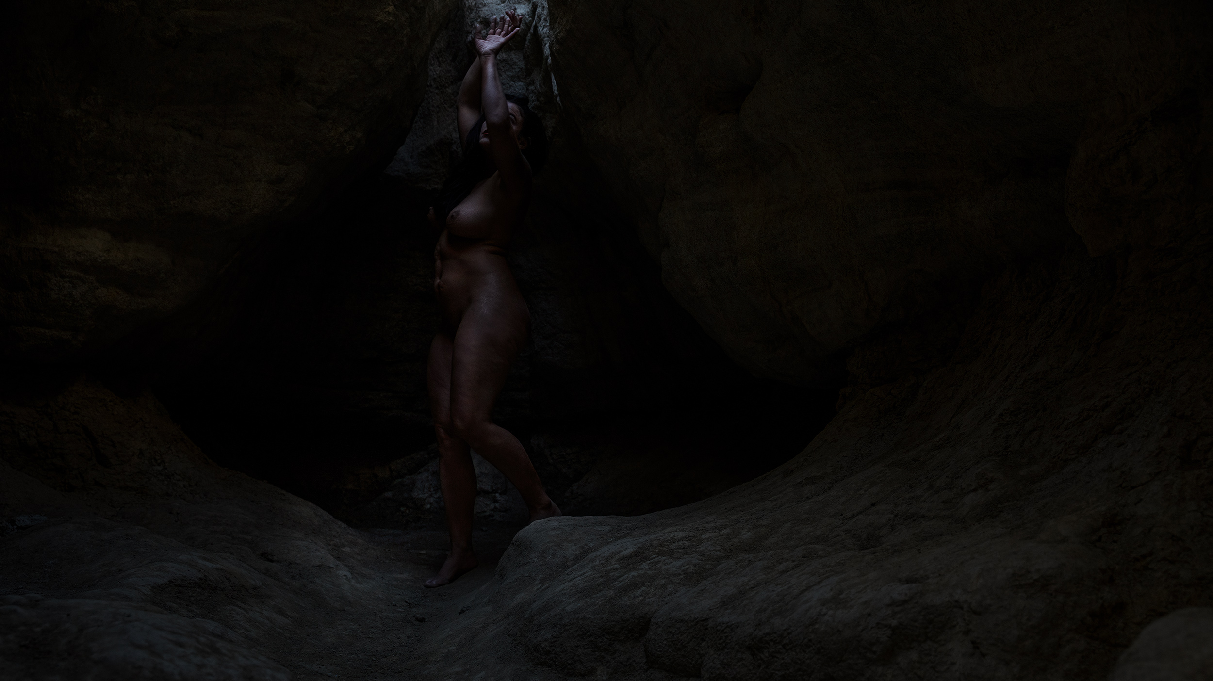 Black and white photo of a woman in a cave nude