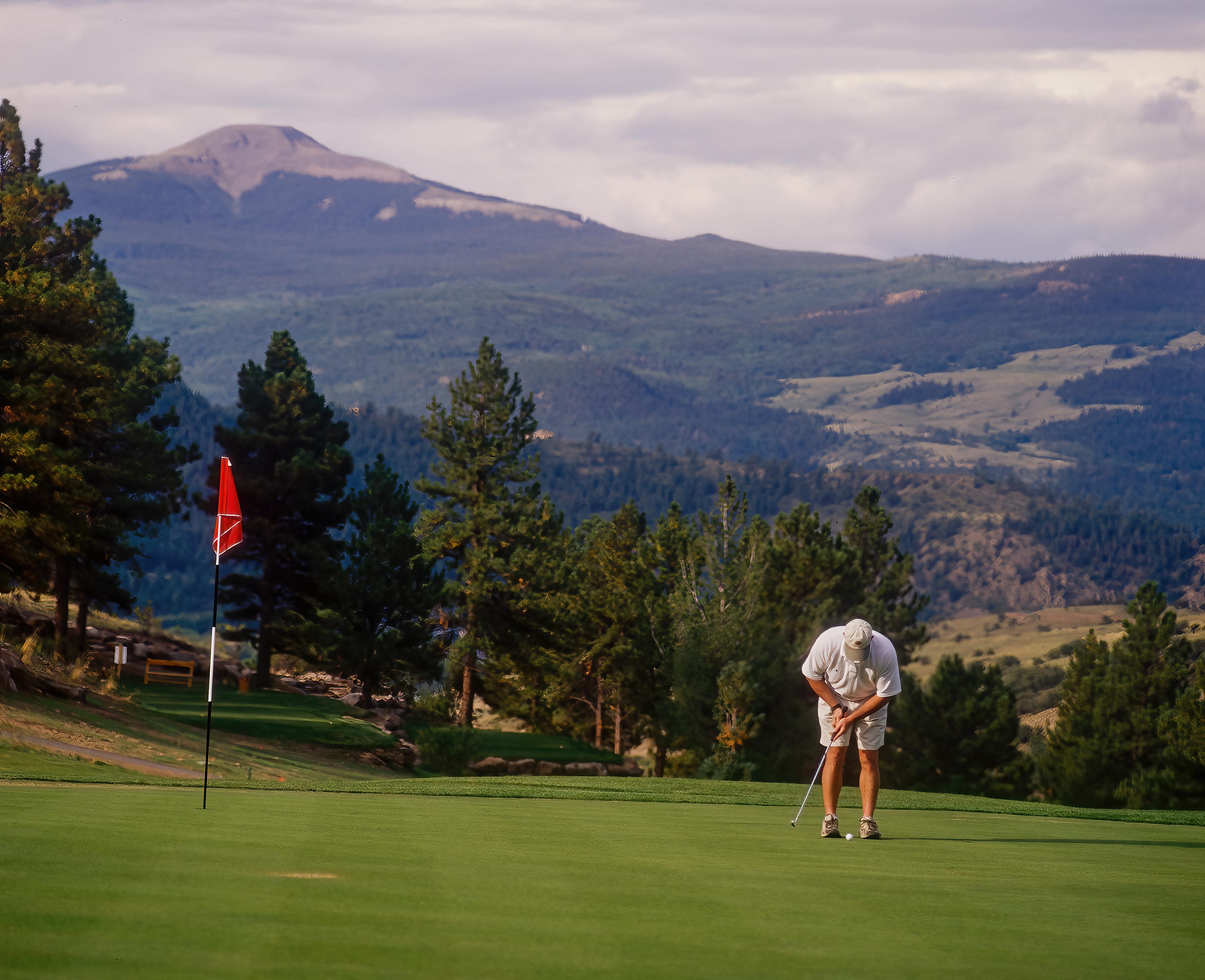 Golfer putting on golf course in mountains.