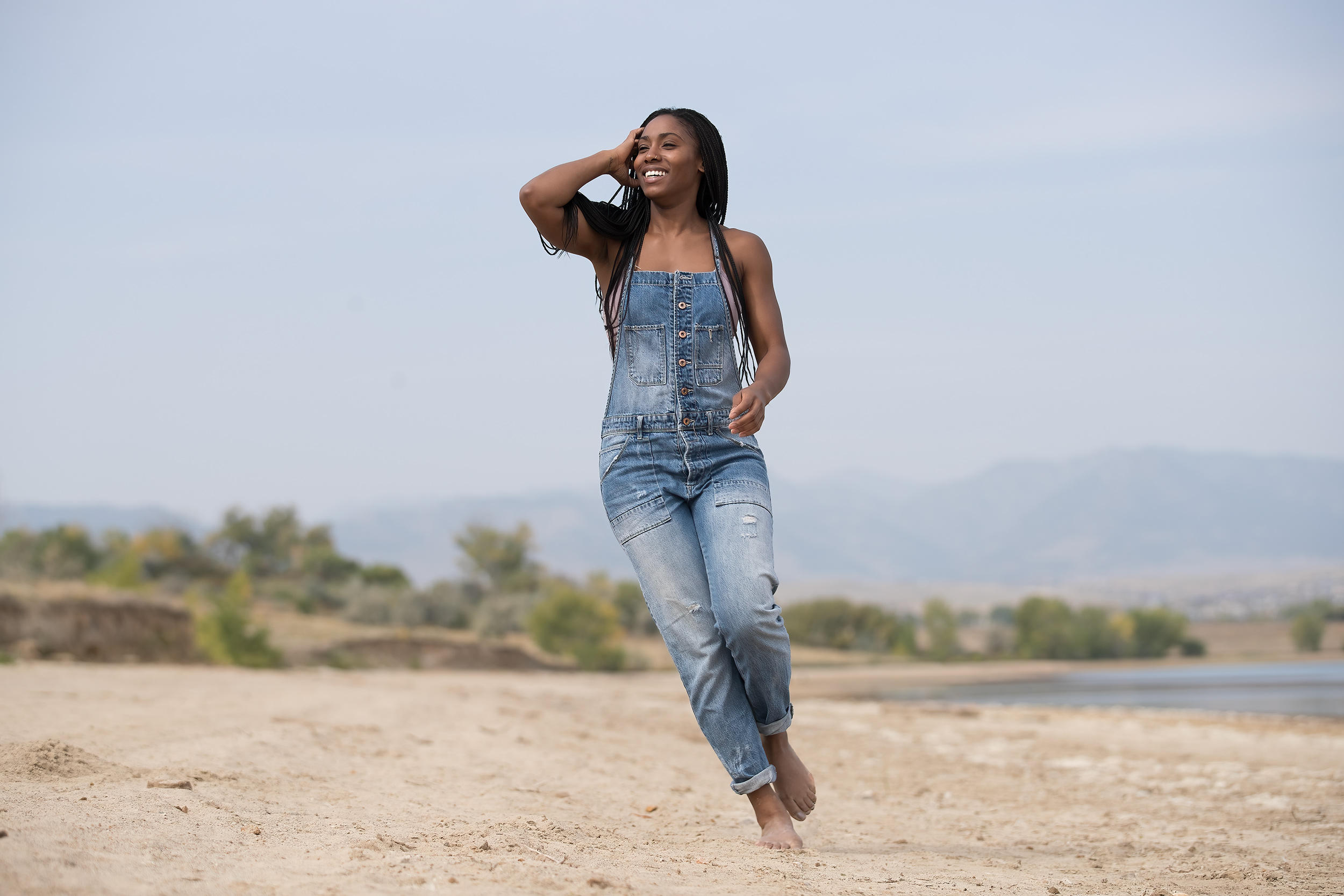 Female model walking on sand near lake with overalls 