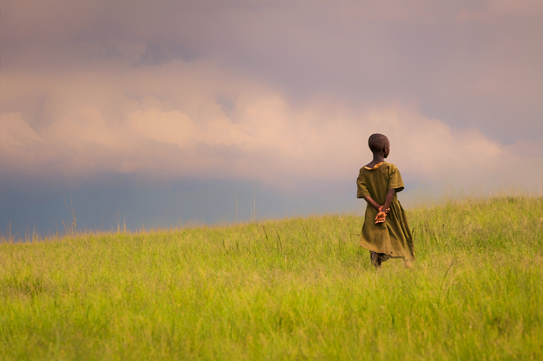 Young african girl standing in a pasture at sunset. 
